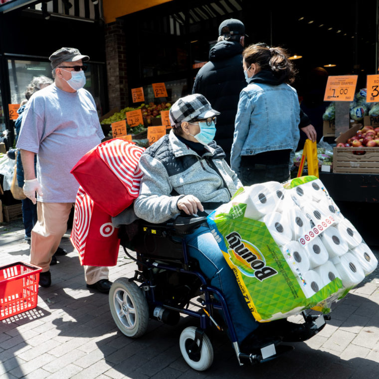 April 25, 2020: Navigating the sidewalk after stocking up on paper towels, 82nd Street at Roosevelt Avenue, Queens, New York. © Camilo José Vergara 